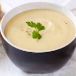 Leek and potato soup in blue bowl garnished with parsley leaves.