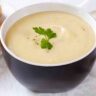 Leek and potato soup in blue bowl garnished with parsley leaves.