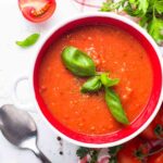 Bowl of tomato soup garnished with fresh basil leaves.