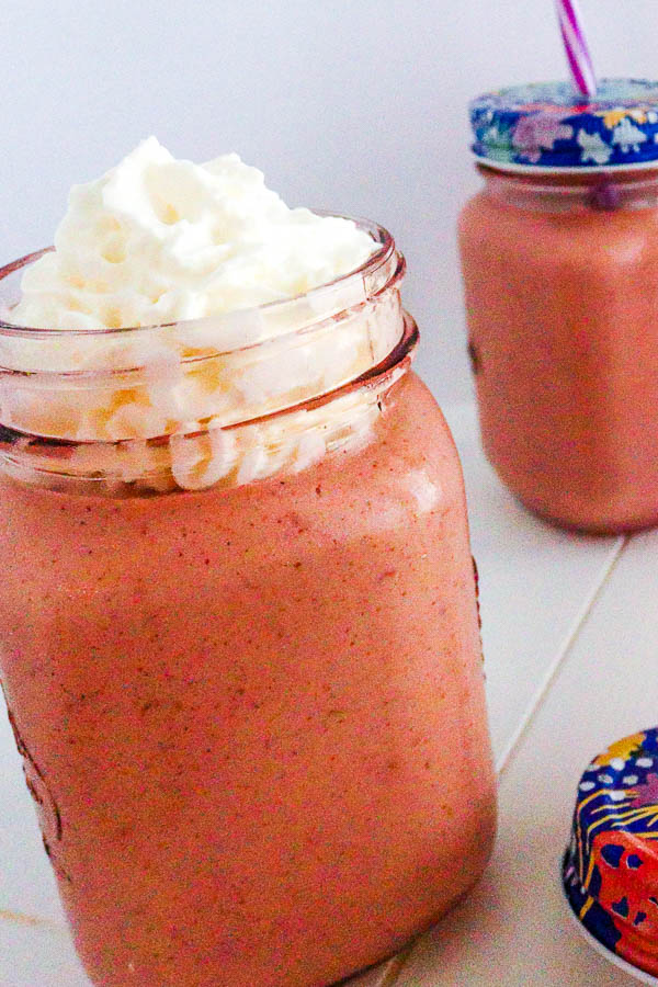 2 pink smoothies in glass jars with whipped cream