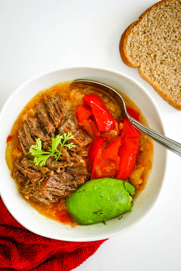 overhead look of bowl with ropa vieja, avocado and red bell pepper with 1 slice of wheat bread