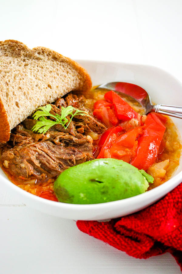 Close up of bowl with ropa vieja, avocado, sliced red bell pepper and bread slice