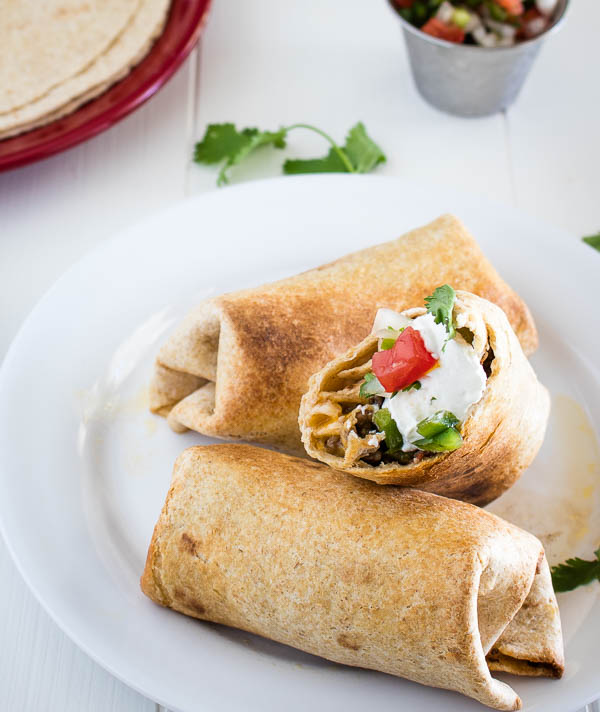 3 grilled stuffed burritos with one bitten into and topped with sour cream and pico de gallo