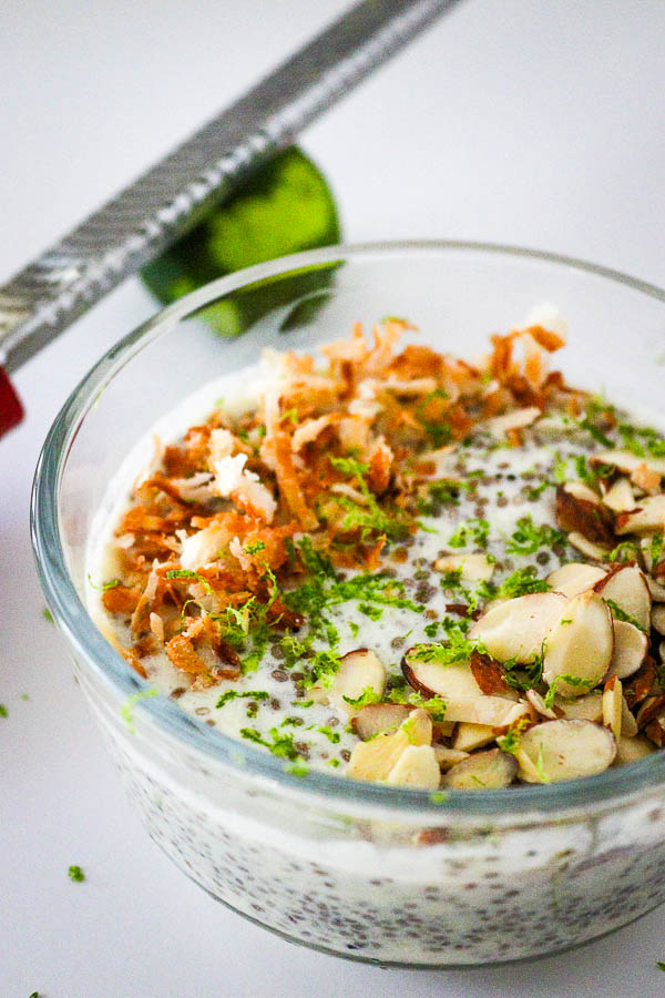 Healthy Pina Colada Chia Pudding in glass bowl topped with toasted coconut, almonds and lime zest