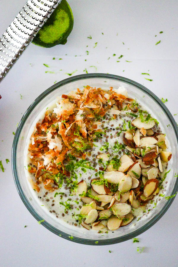 Healthy Pina Colada Chia Pudding in glass bowl topped with toasted coconut, almonds and lime zest overhead look 1