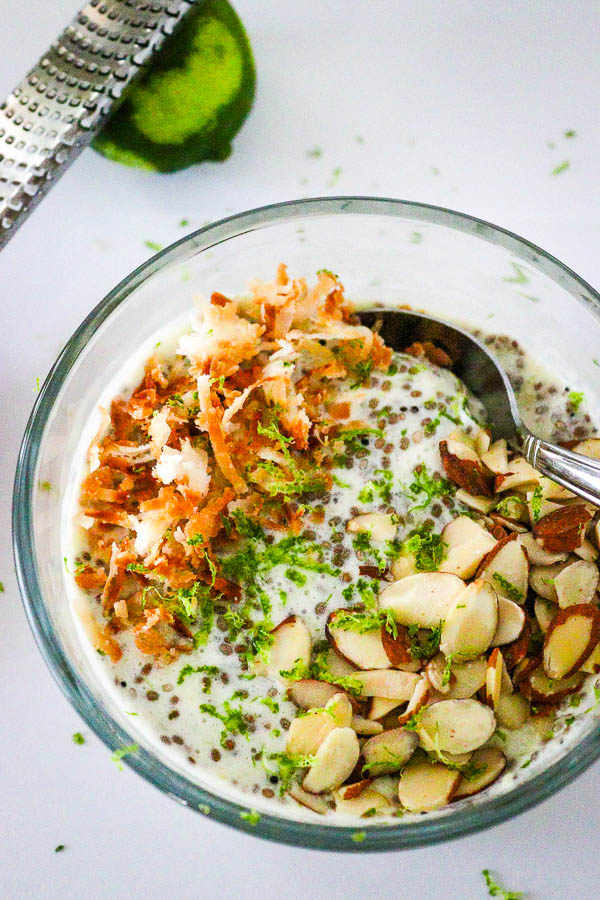 Healthy Pina Colada Chia Pudding in glass bowl topped with toasted coconut, almonds and lime zest overhead look 2