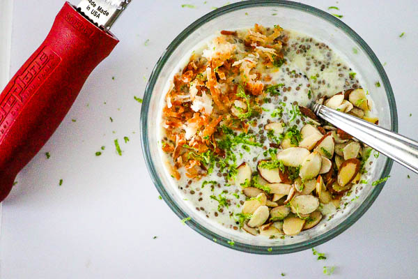 Healthy Pina Colada Chia Pudding in glass bowl topped with toasted coconut, almonds and lime zest overhead look horizontal