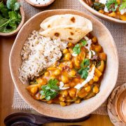 Chickpea curry in bowl with rice and naan, garnished with coconut milk and cilantro.