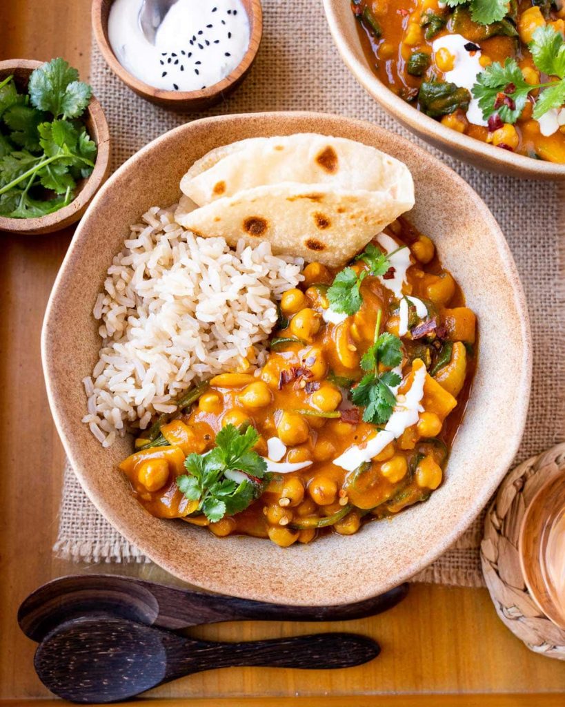 Chickpea curry in bowl with rice and naan, garnished with coconut milk and cilantro.