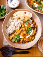Chickpea curry in bowl with rice and naan, garnished with coconut milk and cilantro.