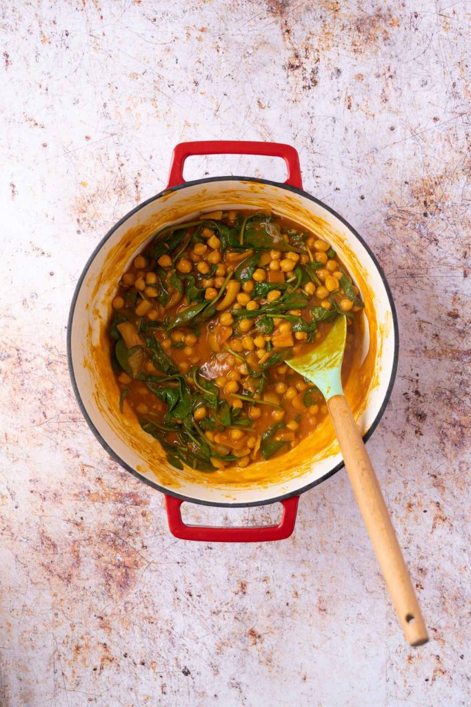 Chickpeas and wilted spinach for curry in pot.