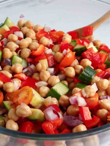 Chickpea salad mixed in a bowl with a wooden spoon.