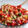 Chickpea salad mixed in a bowl with a wooden spoon.